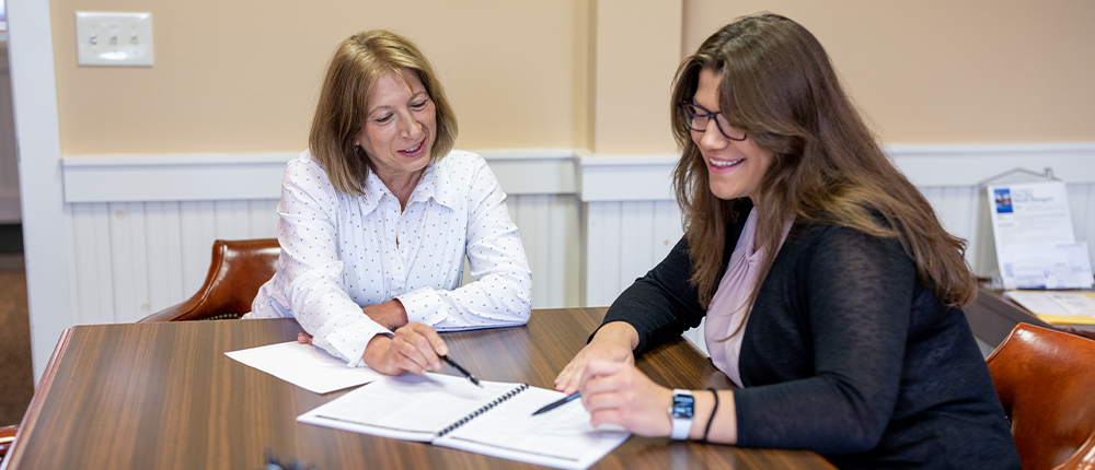 Two female Great Midwest Bank employees review a paper document seated at a wooden table.