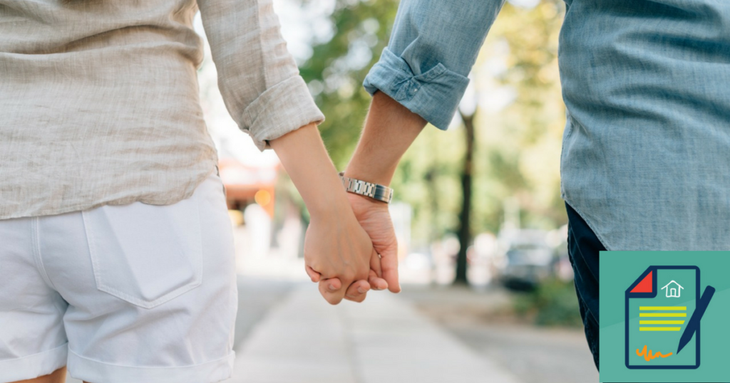 a young couple holds hands while walking down a sidewalk