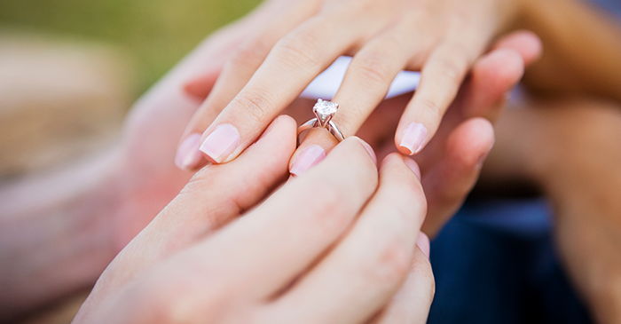 close up of one set of hands placing a diamond engagement ring on another set of hands