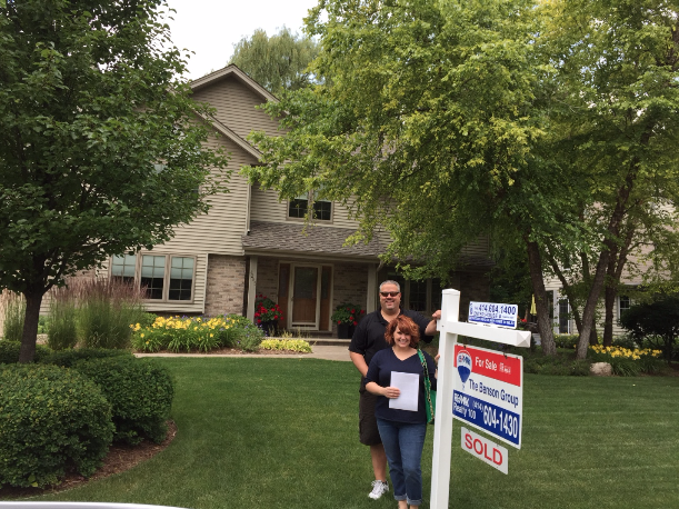 Justin & Nicole stand in their front yard next to a ReMax Realtor "SOLD" sign.