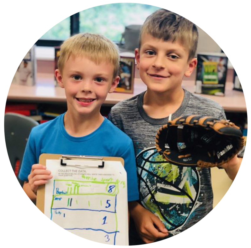 Two young children pose for the camera, one holding a clipboard showing an education activity they were working on while the other holds a baseball mitt.