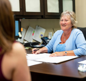 A Great Midwest Bank employee sits behind a desk while smiling and conversing with a customer.
