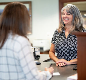 A Great Midwest Bank employee stands at a teller station helping a customer while smiling.