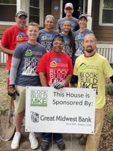 A group of Great Midwest Bank employees stand in front of a house with a sign that reads "Block Build MKE: This house is sponsored by Great Midwest Bank"
