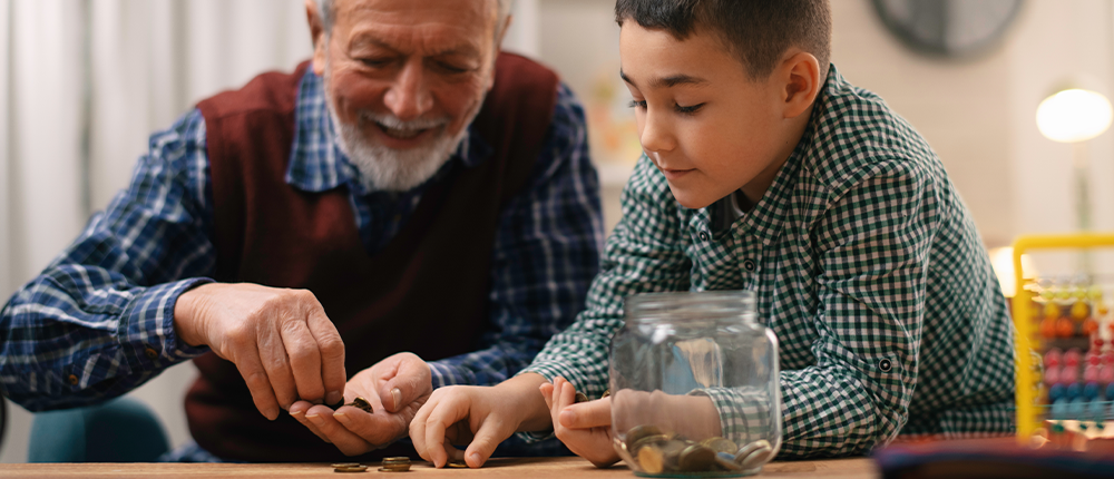 A grandfather counts coins from a jar with his young grandson.